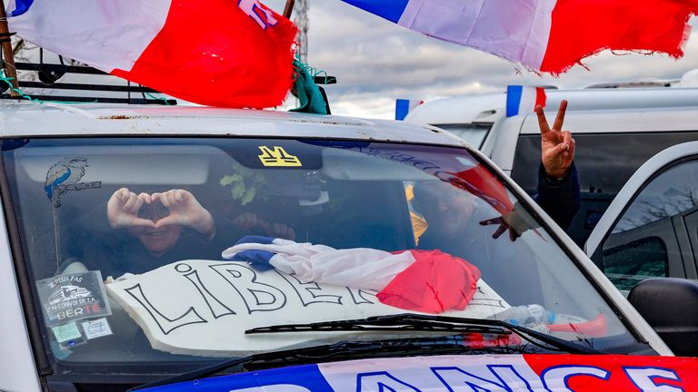 A couple gesture from a car covered in French flags and the message "Liberty" arrive at a car park outside the centre of Brussels. Pic: AP