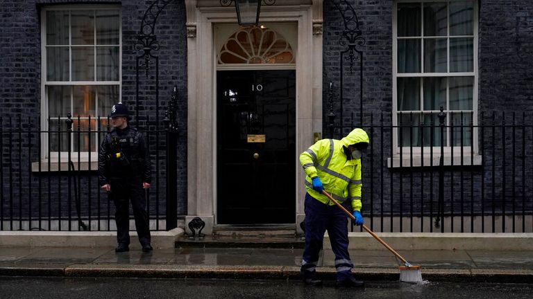 A worker sweeps in the rain and a police officer stands guard outside the door of 10 Downing Street, in London.