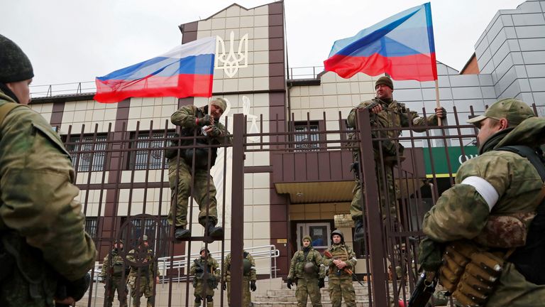 Servicemen of pro-Russian militia hoist flags of Russia and the separatist self-proclaimed Luhansk People&#39;s Republic (LNR) outside the Oschad bank branch in Stanytsia Luhanska in the Luhansk region, Ukraine February 27, 2022. REUTERS/Alexander Ermochenko
