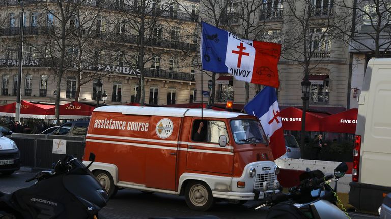 A demonstrator holding a French flag decorated with the Gaullist cross, drives up the Champs-Elysees avenue during a protest, Saturday, Feb.12, 2022 in Paris. Paris police intercepted at least 500 vehicles attempting to enter the French capital in defiance of a police order to take part in protests against virus restrictions inspired by the Canada's horn-honking "Freedom Convoy." . (AP Photo/Adrienne Surprenant)