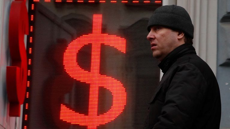 A man walks past a board showing the U.S. dollar sign in a street in Saint Petersburg