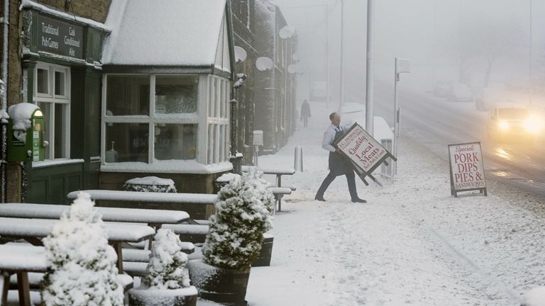 A local butcher carries his shop sign across a snowy pavement in Tow Law, County Durham, as Storm Eunice sweeps across the UK after hitting the south coast earlier on Friday. With attractions closing, travel disruption and a major incident declared in some areas, people have been urged to stay indoors. Picture date: Friday February 18, 2022.