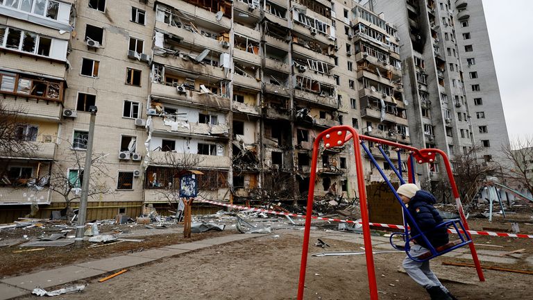 A child sits on a swing in front of a damaged residential building, after Russia launched a massive military operation against Ukraine, in Kyiv, Ukraine February 25, 2022. REUTERS/Umit Bektas
