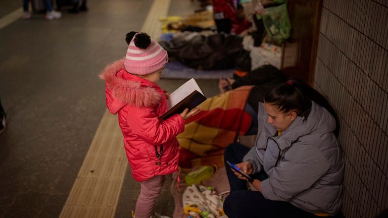A girl looks at a notebook next to her mother as they stand in the Kyiv subway, using it as a bomb shelter, Ukraine, Saturday Feb. 26, 2022. (AP Photo/Emilio Morenatti)