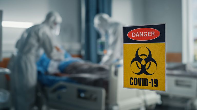 Hastane Coronavirus Acil Servis Koğuşu: Tulum giyen doktorlar, Yüz Maskeleri Hastaları Tedavi Ediyor, İyileştiriyor ve Hayat Kurtarıyor.  Kapıdaki Biyolojik Tehlike İşaretine Odaklanın, Arka Plan Odak Dışı Bulanık