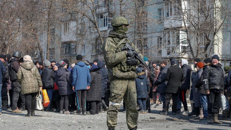 A Russian army soldier stands next to local residents who queue for humanitarian aid delivered during Ukraine-Russia conflict, in the besieged southern port of Mariupol, Ukraine March 23, 2022.  REUTERS/Alexander Ermochenko