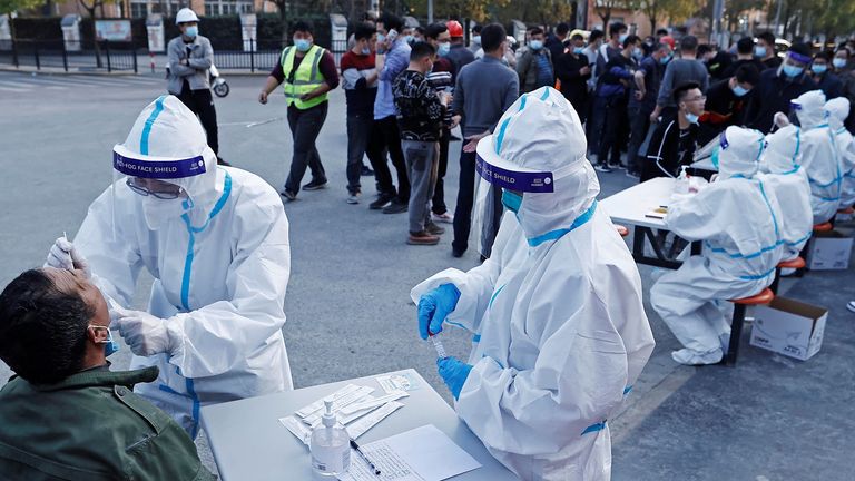 A medical worker in protective suit collects a swab from a resident at a makeshift nucleic acid testing site