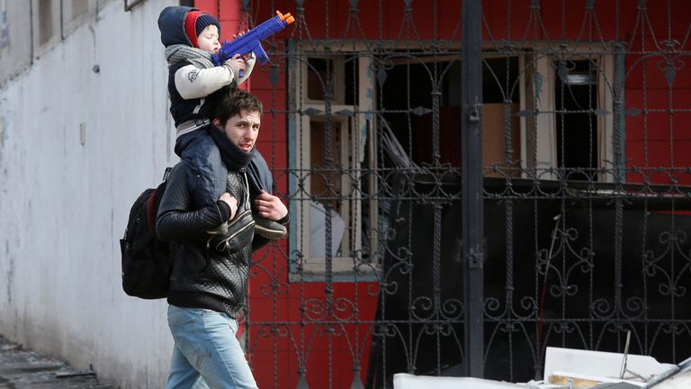 A child sits on the shoulders of a man near a building damaged in Mariupol