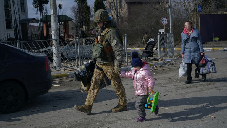 A member of the military holds the hand of a child as people flee, amid Russia&#39;s invasion of Ukraine, in Romanivka, Ukraine, March 9, 2022. REUTERS/Maksim Levin
