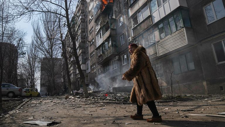 A woman walks past a burning apartment building in Mariupol. Pic: AP