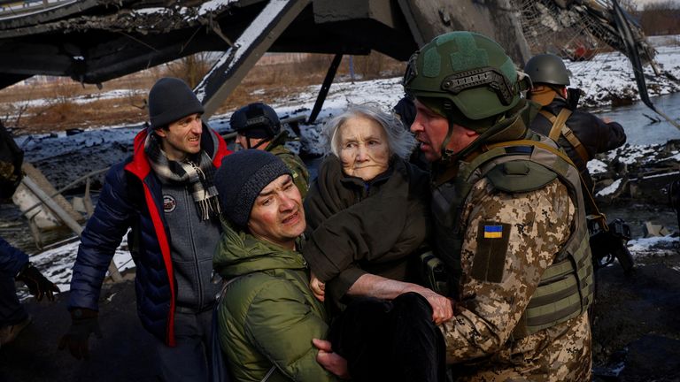 Two men carry a woman as people flee from advancing Russian troops in the town of Irpin outside Kyiv