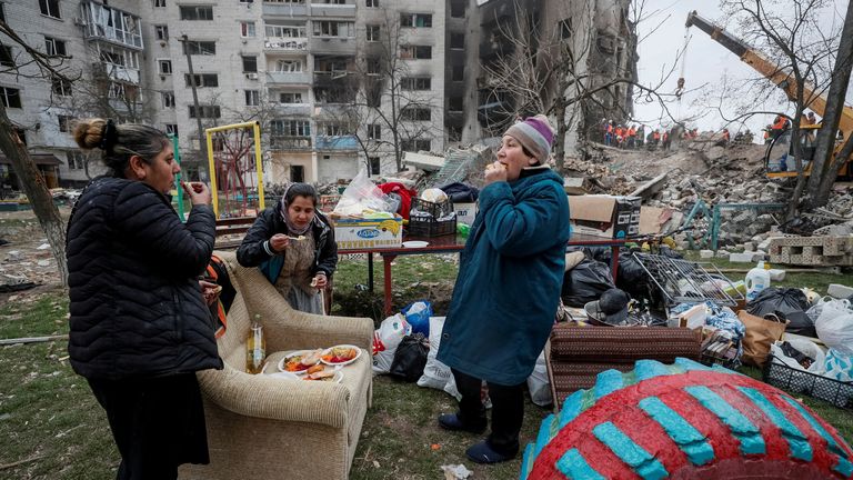 Miejscowi jedzą darmowe jedzenie w pobliżu ich domu zniszczonego przez rosyjskie bombardowanie w Borodince