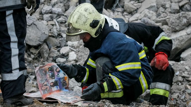 Ratownik ogląda album ze zdjęciami znaleziony w gruzach bloku mieszkalnego zniszczonego przez rosyjskie bombardowanie w Borodince