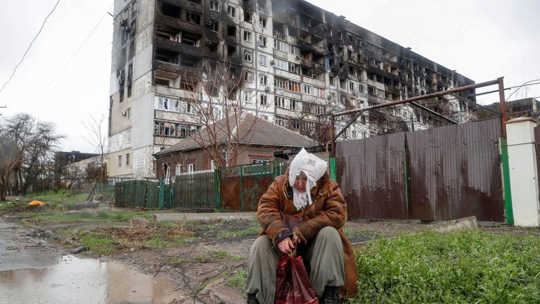 An elderly woman sits outside a badly damaged building in Mariupol