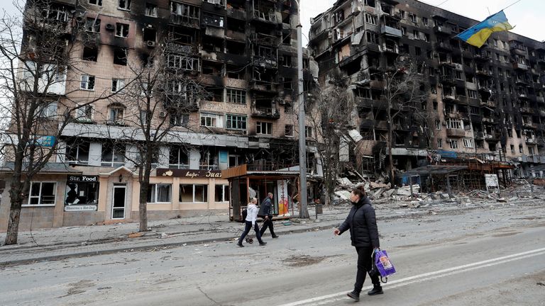 Les gens marchent le long d'une rue près d'un drapeau ukrainien déchiré, qui est accroché à un fil devant un immeuble d'appartements détruit pendant le conflit Ukraine-Russie, dans la ville portuaire méridionale de Mariupol, Ukraine le 14 avril 2022. REUTERS/Alexander Ermochenko
