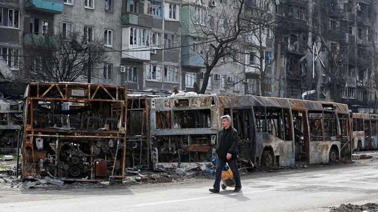 Un résident local marche le long d'une rue devant des bus incendiés pendant le conflit Ukraine-Russie dans la ville portuaire méridionale de Marioupol, Ukraine le 19 avril 2022. REUTERS/Alexander Ermochenko
