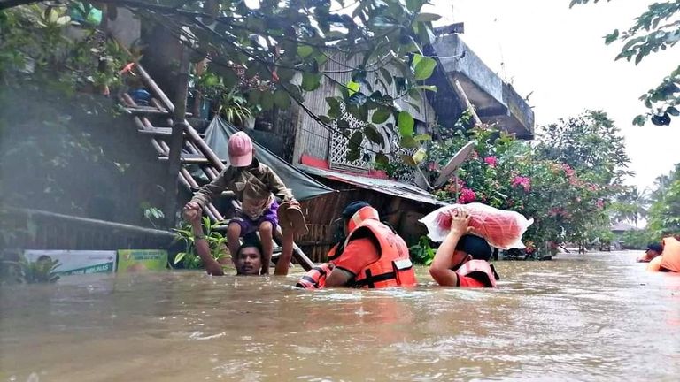 A man carries a boy on his shoulder as they walk through a flooded road along with rescue personnel, after the tropical storm Megi hit, in Capiz Province, Philippines April 12, 2022. Philippine Coast Guard/Handout via REUTERS THIS IMAGE HAS BEEN SUPPLIED BY A THIRD PARTY. MANDATORY CREDIT. NO RESALES. NO ARCHIVES
