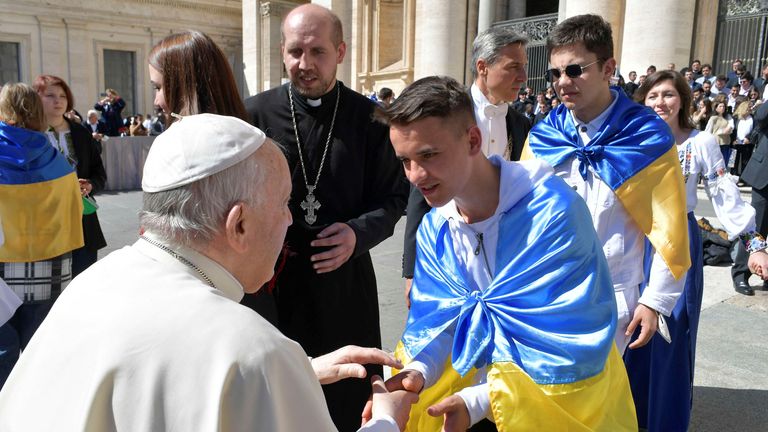 Paus Fransiskus berjabat tangan dengan pemuda yang dibungkus bendera Ukraina selama audiensi mingguan di Lapangan Santo Petrus di Vatikan.