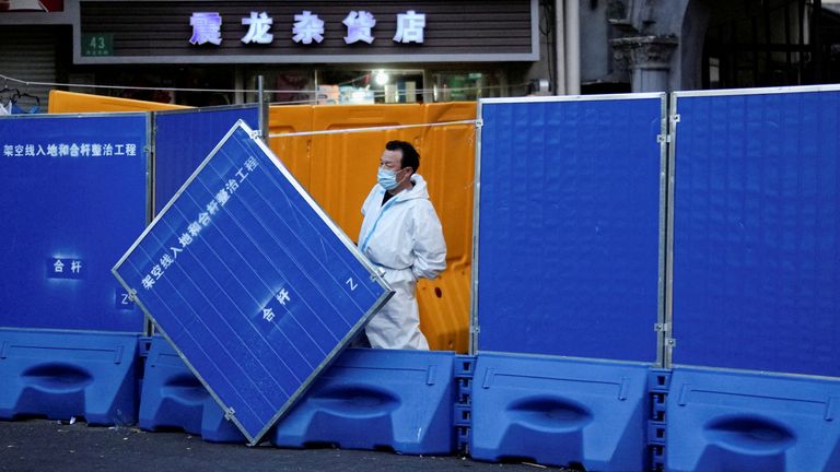 A worker in a protective suit keeps watch next to barricades set around a sealed-off area during the lockdown in Shanghai, China