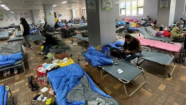 People are sleeping in sleeping bags on top of sun loungers in a communal room 