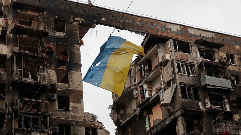 Widok pokazuje rozdartą ukraińską flagę wiszącą na drucie przed budynkiem mieszkalnym zniszczonym podczas konfliktu między Ukrainą a Rosją w południowym mieście portowym Mariupol na Ukrainie 14 kwietnia 2022 r. REUTERS / Aleksander Ermoszenko