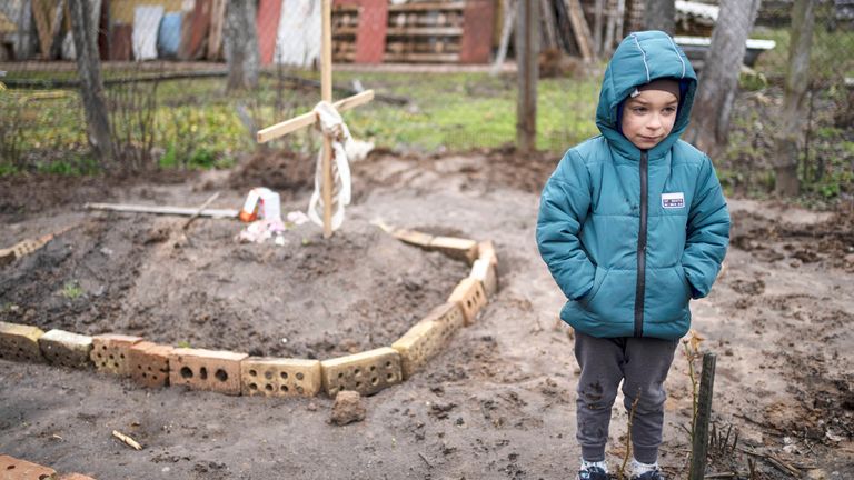 In the courtyard of their house, Vlad Tanyuk, 6, stands near the grave of his mother Ira Tanyuk, who died because of starvation and stress due to the war, on the outskirts of Kyiv, Ukraine, Monday, April 4, 2022. (AP Photo/Rodrigo Abd)