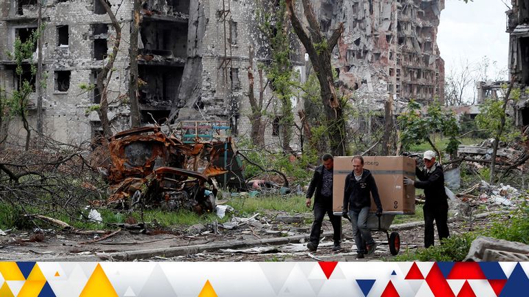 Local residents transport a box on a wheelbarrow past a heavily damaged apartment building near Azovstal Iron and Steel Works, during Ukraine-Russia conflict in the southern port city of Mariupol, Ukraine May 22, 2022. REUTERS/Alexander Ermochenko