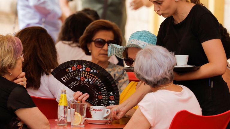 A tourist uses a fan to cool off as a waitress serves at the terrace of a bar during an episode of exceptionally high temperatures for the time of year in Ronda, Spain, May 20, 2022. REUTERS/Jon Nazca
