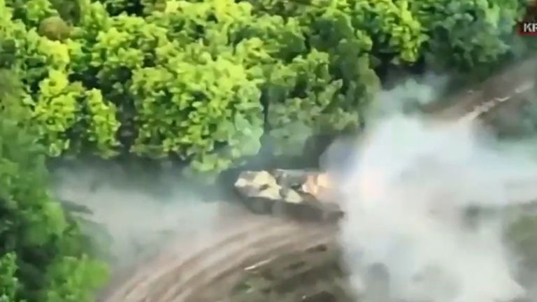 Still from aerial footage appearing to show foreign fighters including Ben Grant, son of a UK MP, ambushing a Russian armoured troop carrier. The troop carrier smokes as it leaves the scene with flashes on its exterior appearing to show secondary explosions from detonating ammunition