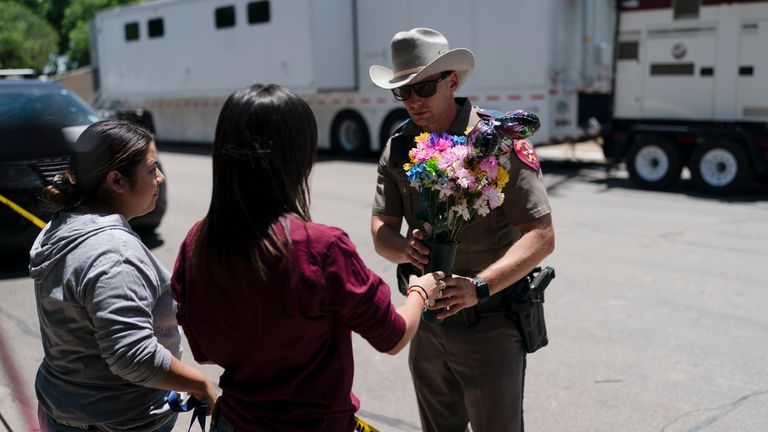 A state trooper picks up flowers to place on a makeshift memorial honoring victims killed at Robb Elementary School