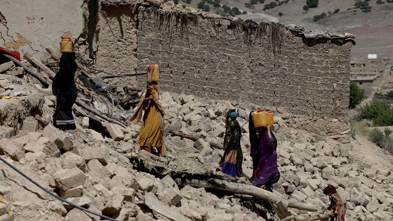 Afghan women carry water containers through the debris of damaged houses in Wor Kali