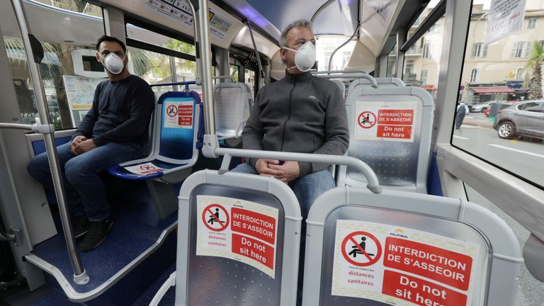 People wear face masks on a bus with social distancing signs on seats in Cannes