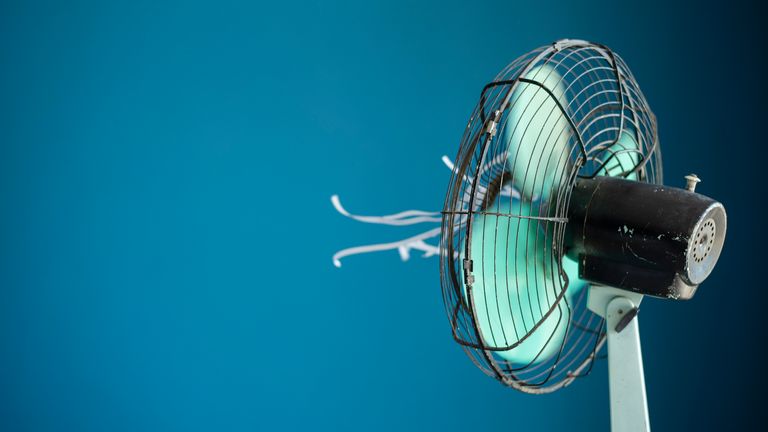 Shot of a metal electric fan with white streamers attached against a blue background


