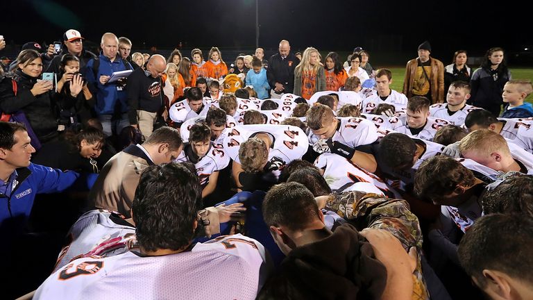 Bremerton's assistant football coach Joe Kennedy, obscured in center in blue, is surrounded by Centralia High School football players who kneel on the field and pray with him after their game against Bremerton October 16, 2015 in Bremerton, Washington.  After losing his coaching job for refusing to kneel in prayer with players and spectators on the field immediately after football matches, 