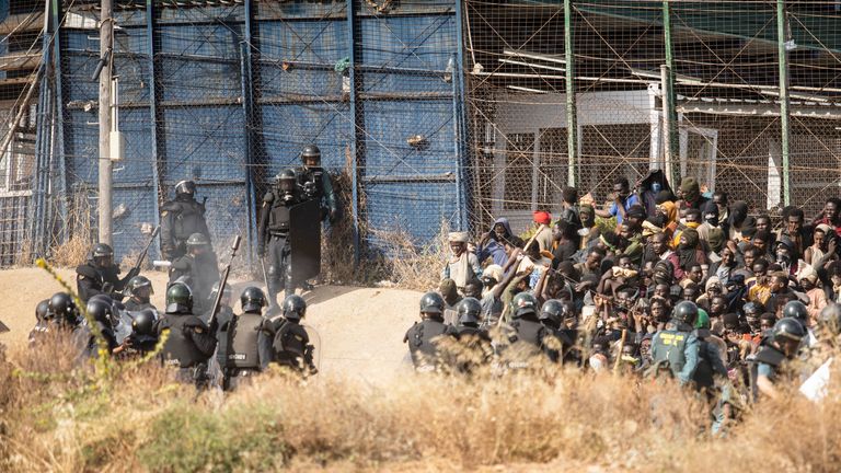 Riot police officers, left, cordon off the area after migrants arrive on Spanish soil and crossing the fences separating the Spanish enclave of Melilla from Morocco in Melilla, Spain, Friday, June 24, 2022. Dozens of migrants stormed the border crossing between Morocco and the Spanish enclave city of Melilla on Friday in what is the first such incursion since Spain and Morocco mended diplomatic relations last month. (AP Photo/Javier Bernardo)