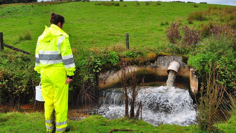 An Environment Agency employee inspects the outfall at the River Inny. 