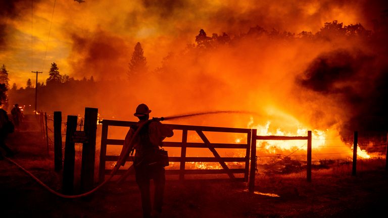 Ein Feuerwehrmann löscht Flammen, als Oak Fire die Dara Road überquert.  in Mariposa County, Kalifornien, Freitag, 22. Juli 2022. Die Besatzungen konnten sie daran hindern, zu einem nahe gelegenen Haus zu gelangen.  (AP Foto/Noah Berger)