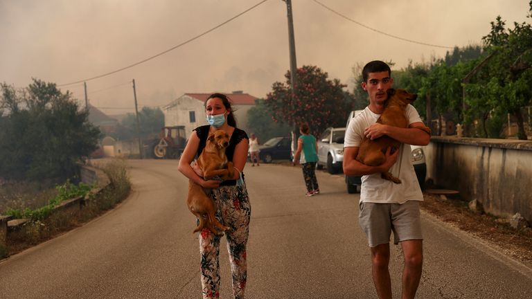 Orang-orang membawa anjing mereka saat mereka mengungsi setelah kebakaran hutan, di Leiria, Portugal 13 Juli 2022. REUTERS/Rodrigo Antunes