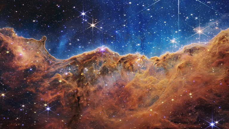 What looks like craggy mountains on a moonlit evening is actually the edge of a young star-forming region, nearby NGC 3324 in the Carina Nebula.  Captured in infrared light by the Near Infrared Camera (NIRCam) on NASA's James Webb Space Telescope, this image shows previously obscured regions of star formation.