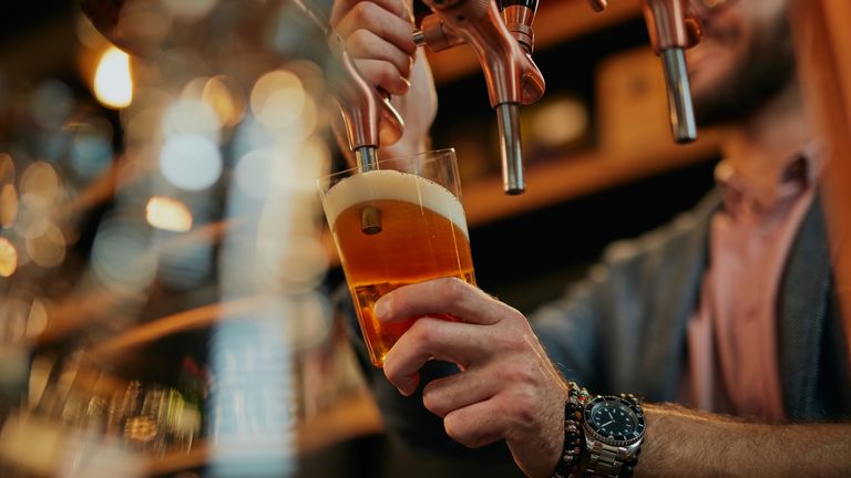 Tattooed caucasian barman pouring beer while standing in pub.