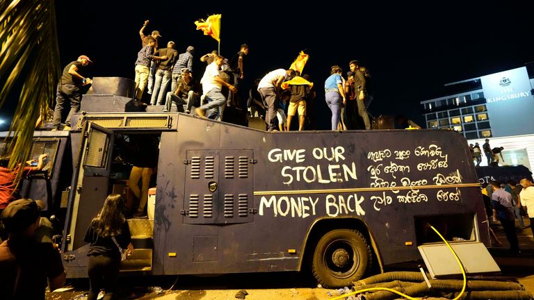 Protestocular Cumartesi günü cumhurbaşkanının resmi konutunun girişinde vandalize edilmiş bir polis tazyikli su kamyonunun üzerinde duruyorlar.  Resim: AP