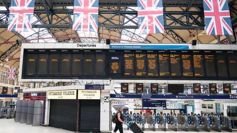 A man crosses a departures sign at Victoria Station in London, as train services continue to be disrupted following a nationwide strike by members of the Rail, Maritime and Transport union along with London Underground workers in a bitter dispute over pay, employment and conditions.