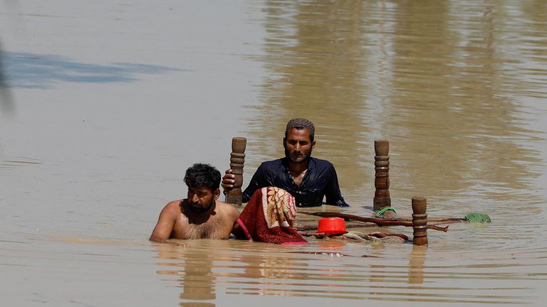 Des hommes traversent les eaux de crue avec leurs effets personnels à Charsadda, au Pakistan, le 28 août 2022. REUTERS/Fayaz Aziz