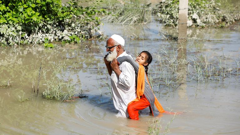 A man wades through flood waters carrying his grand daughter on his back following rains and floods during the monsoon season in Charsadda, Pakistan August 28, 2022. REUTERS/Fayaz AzizAziz