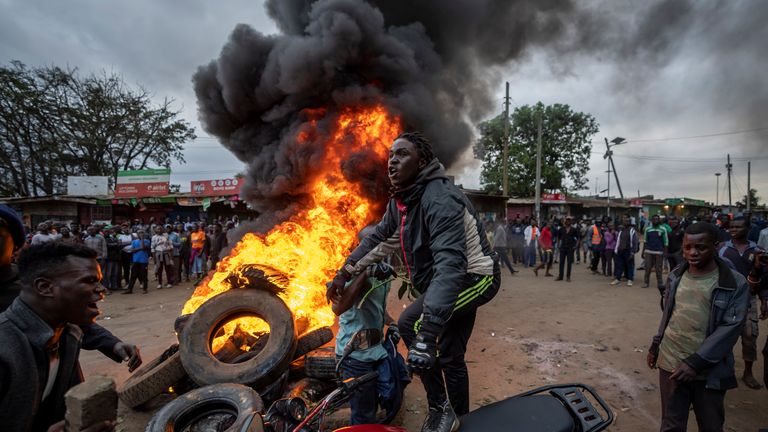 Başkan adayı Raila Odinga'nın bir destekçisi, 15 Ağustos 2022 Pazartesi, Kenya, Nairobi'nin Kibera semtinde, lastik yanan bir barikatı yanında protesto ederken motosikleti üzerinde duruyor. Kenya'nın seçim komisyonu başkanı, yakın cumhurbaşkanlığı seçimlerini beş kez rakip olan Raila Odinga'nın galibi olarak Başkan Yardımcısı William Ruto'yu ilan etti.  (AP Fotoğrafı/Ben Curtis)