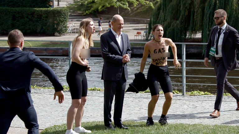 Topless protesters stand next to Olaf Scholz. Pic: AP