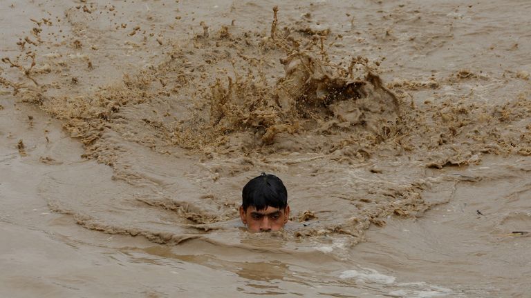 A man swims in flood waters while heading for a higher ground in Charsadda
