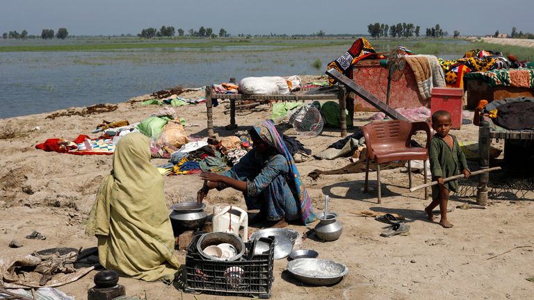 Gari Yasin, Shikarpur, Pakistan'da 31 Ağustos 2022'de muson mevsimi boyunca yağmur ve sel baskınlarının ardından daha yüksek bir yere sığınan kadınlar, eşyalarının yanında yemek hazırlıyor. REUTERS/Akhtar Soomro