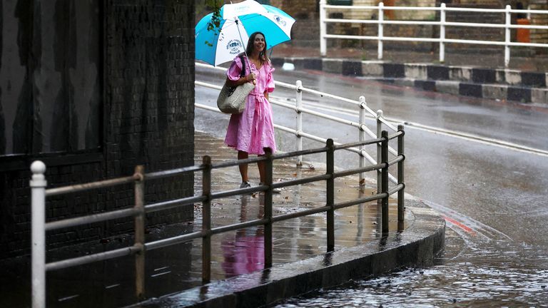 A pedestrian carrying an umbrella walks along a flooded street of a residential area after heavy rain hits London, Britain August 25, 2022. REUTERS/Hannah Mckay