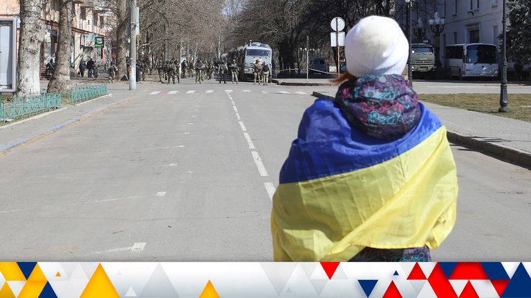FILE - A woman covered by Ukrainian flag stands in front of Russian troops in a street during a rally against Russian occupation in Kherson, Ukraine, on March 19, 2022 